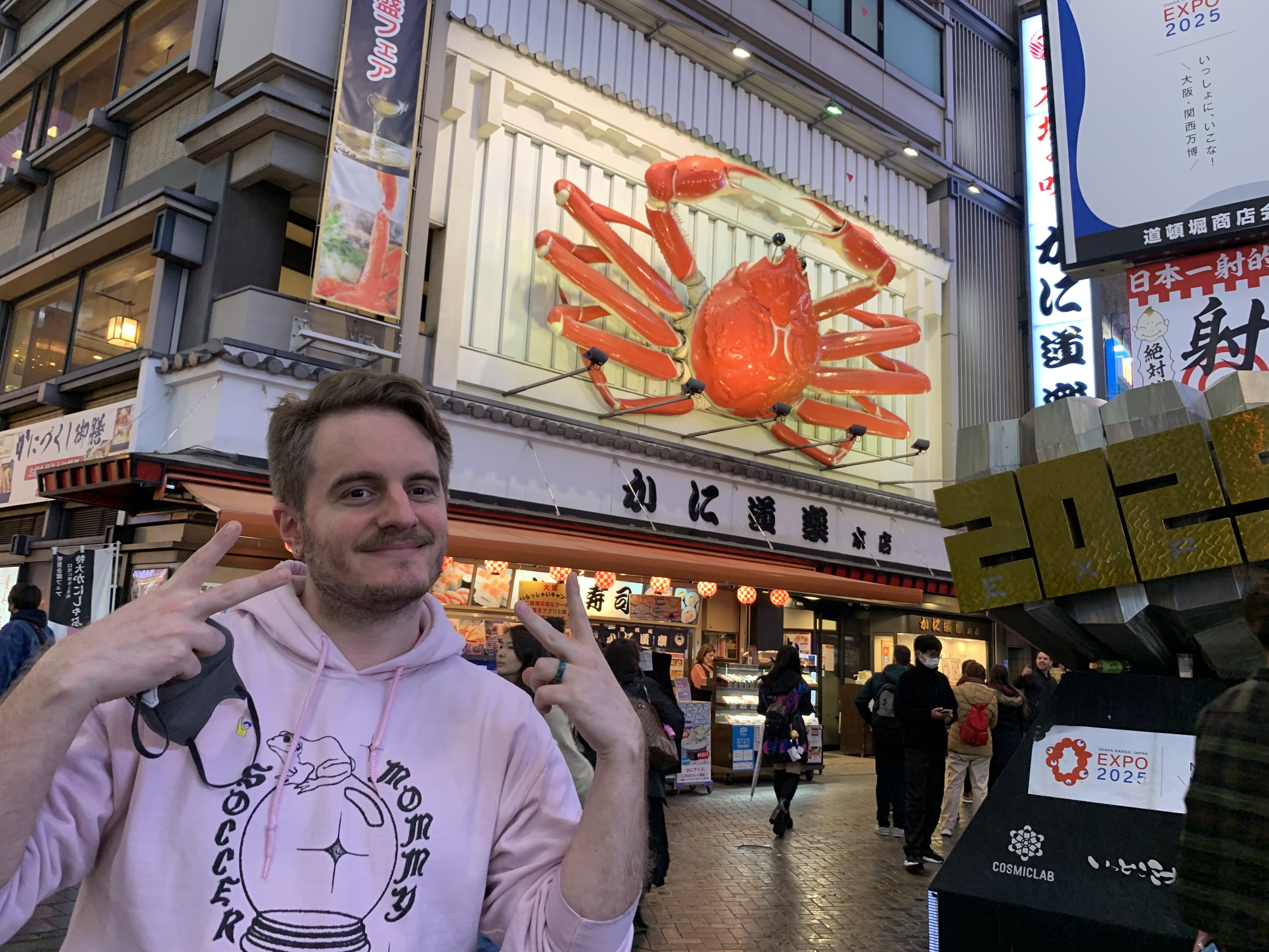 photo of ari throwing up two peace signs and smiling in front of the giant crab in dotonbori, osaka, japan